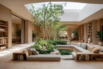 Contemporary reading lounge with a sunken planted courtyard, curved seating, pale oak walls, limestone flooring, and soft skylight illumination.